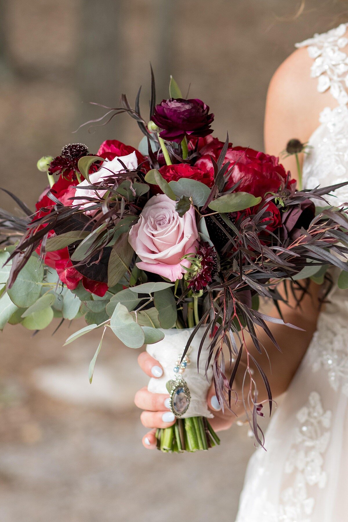 Bridal bouquet of red peonies, blush roses, red roses, burgundy ranunculus and eucalyptus wrapped in an ivory silk ribbon with a small portrait of the bride's grandparents attached.