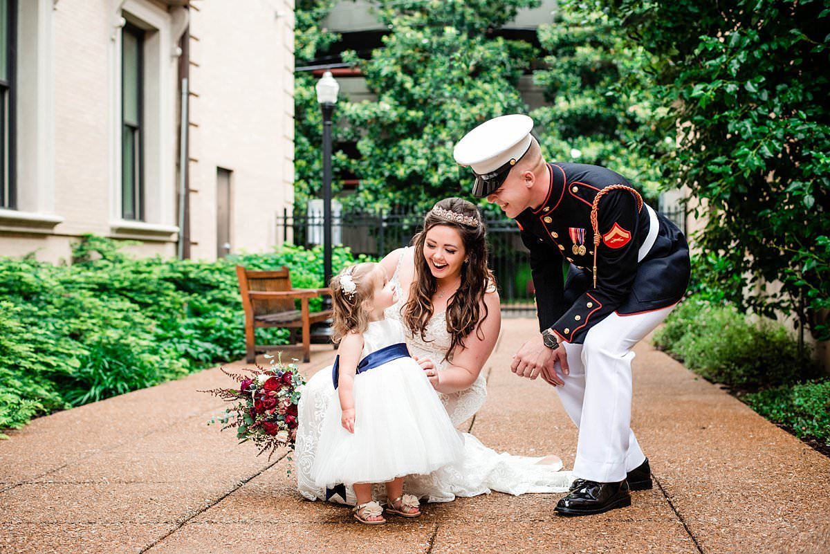 Marine kneeling down to chat with the flower girl and his wife