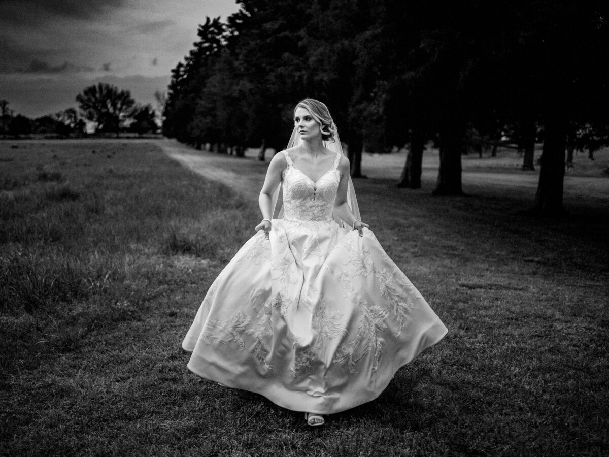 a bride holding up her dress and walking in a field