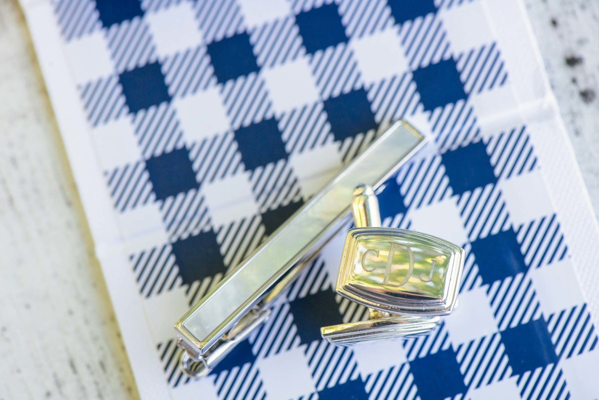 Groom's cufflinks and tie clip on blue plaid background at The Ram's Head Inn