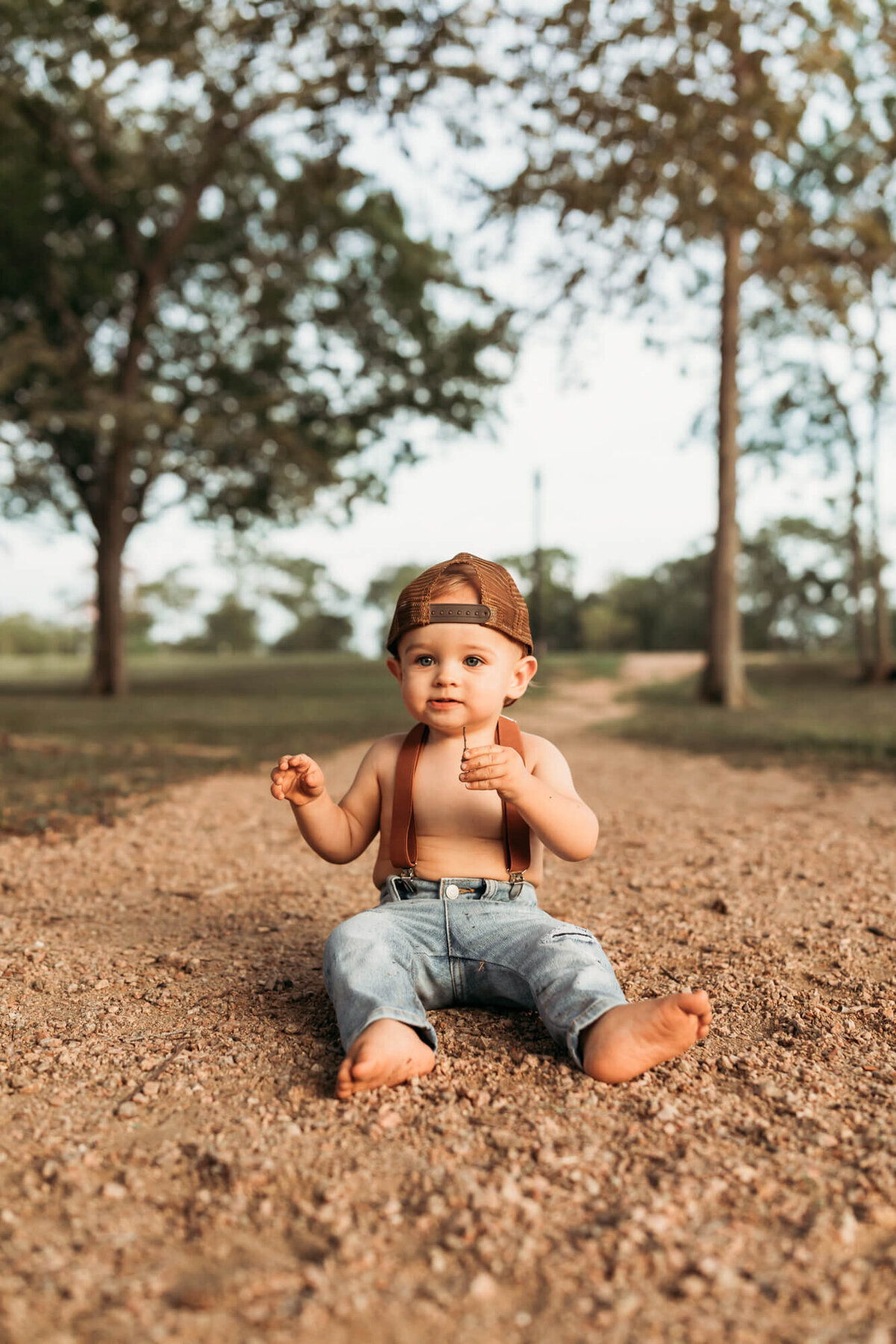 baby boy wears a trucker hat, wearing denim and suspenders