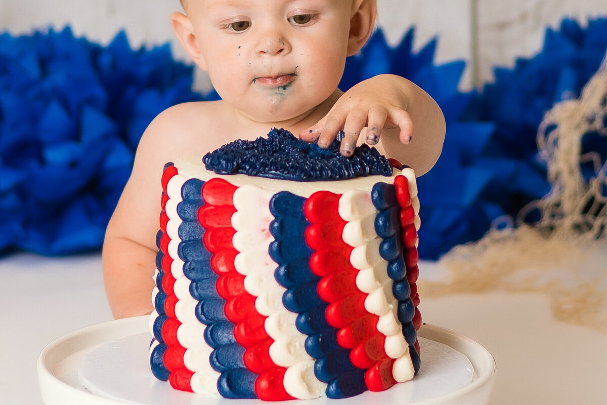 Cake Smash Photographer, a baby eats from a red, white, and blue cake
