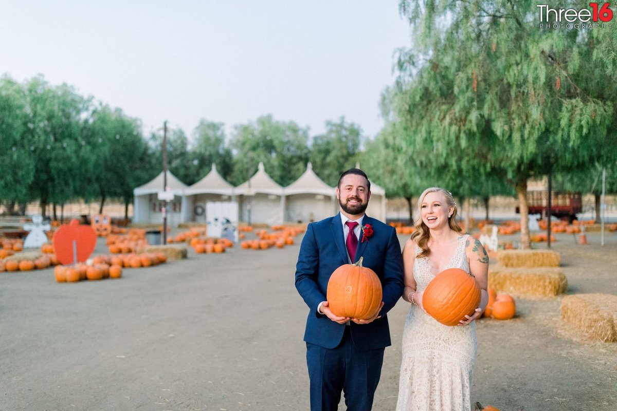 Bride and Groom pose together holding pumpkins