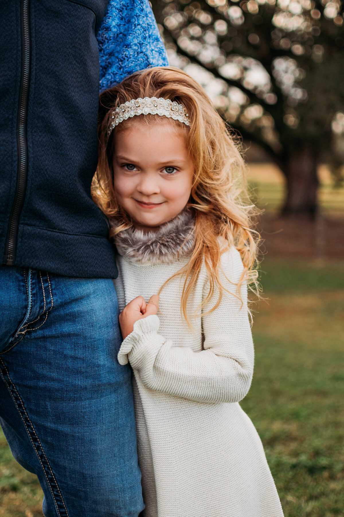 A close up picture of a young girl hugging her dad's leg as she smiles at the camera.