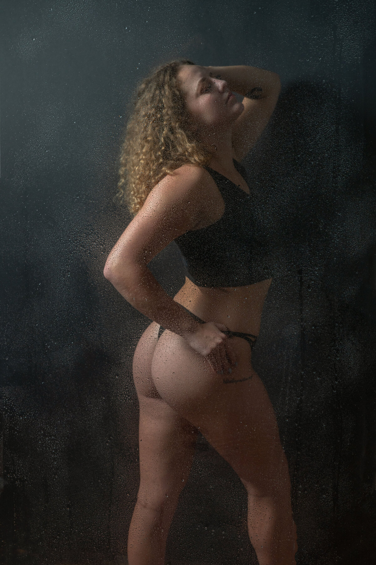 A woman in a black lingerie is pretending she is taking a shower for a boudoir shower scene in Orlando.