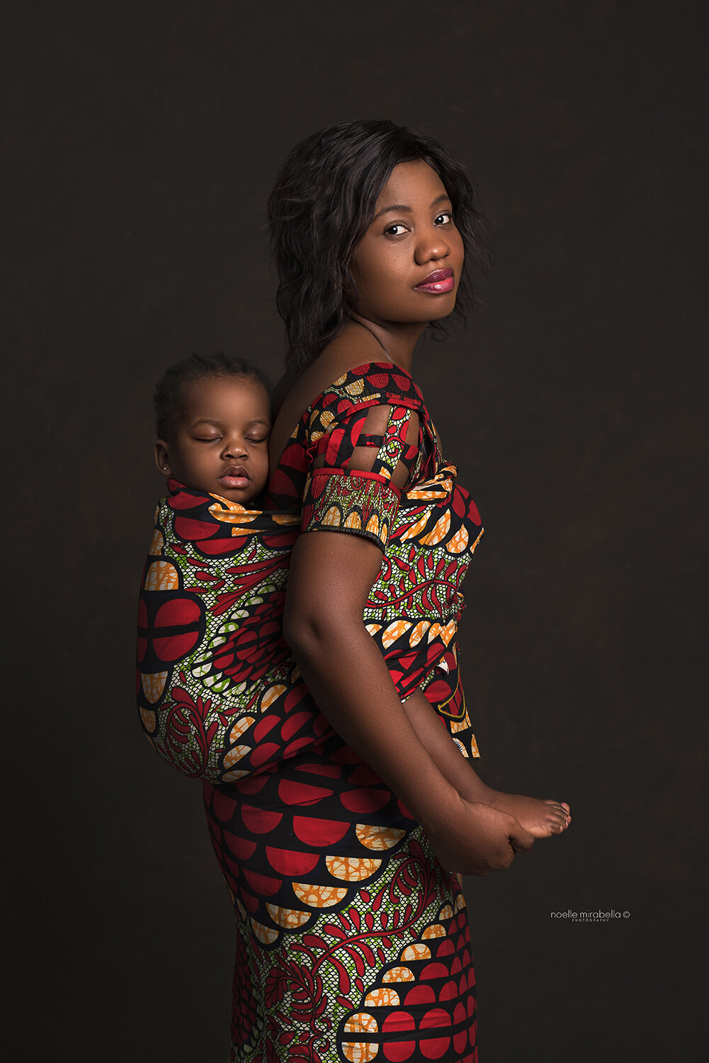 Mother wearing her sleeping baby on her back, dressed in traditional African clothing.