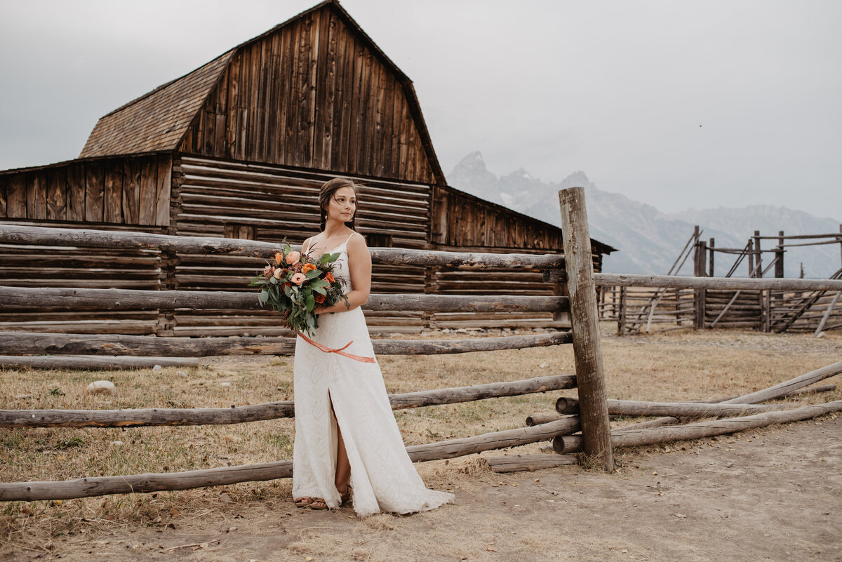 Photographers Jackson Hole capture bride standing in front of barn in wedding dress
