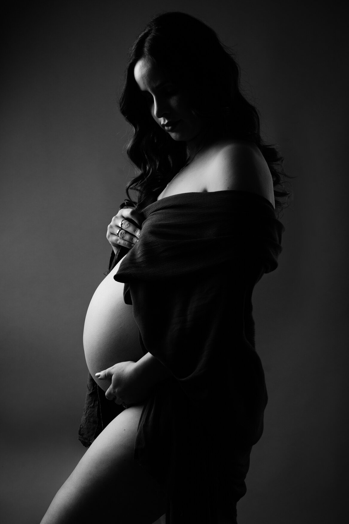 Portrait of a pregnant woman with long curly hair looking down her belly covered only with a dark fabric