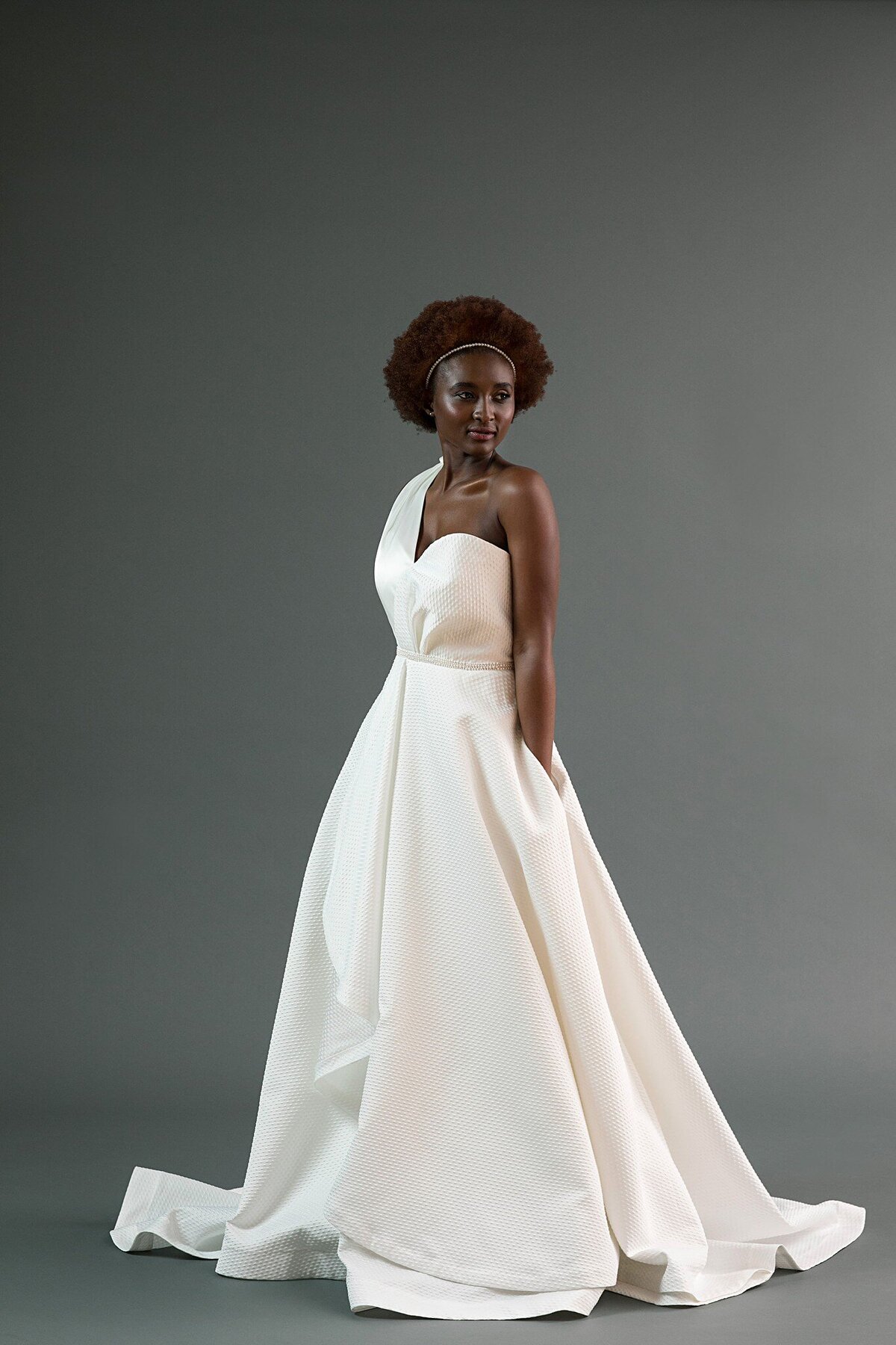 The Kimi bridal style is an a-line, asymmetrical wedding dress with pockets in a textured dot jacquard fabric.