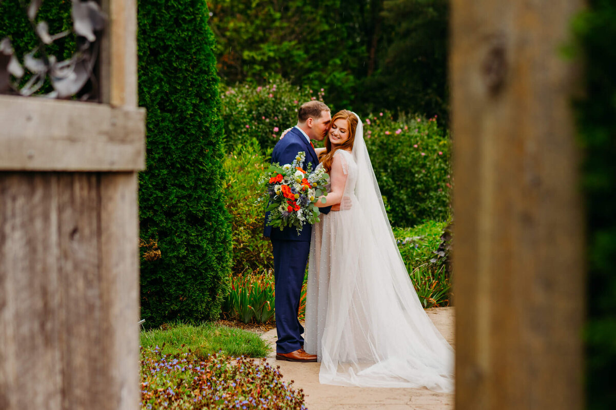 photo of a groom whispering in his brides ear inside of a garden in between wooden doors