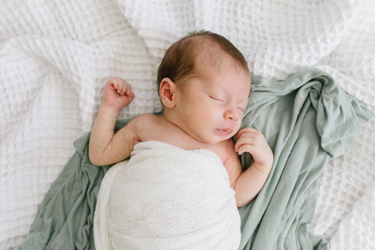 newborn baby swaddled in white and lying on sage green and white blanket