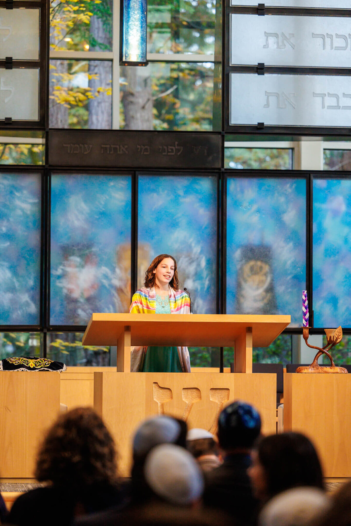 A teen girl in a rainbow tallit standing at the altar performing her haftarah to a full temple taken by a Bellevue Bar and Bat Mitzvah Photography specialist