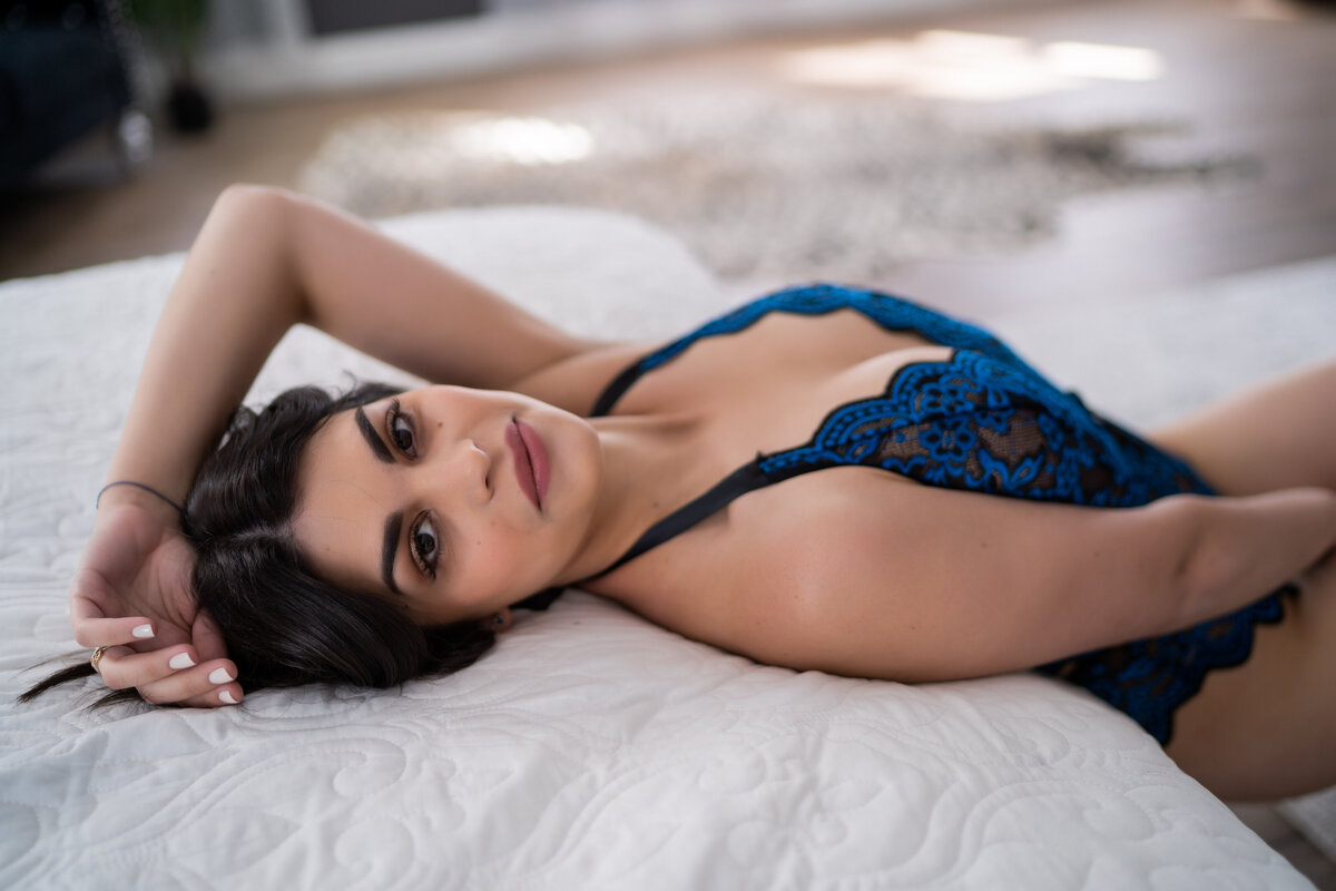 woman leaning on white bed  in blue lingerie posing for camera