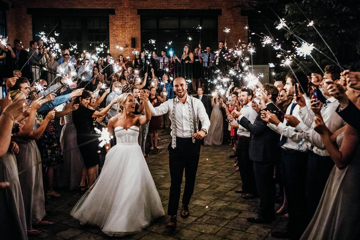 Bride and groom walking out of wedding ceremony with guests holding sparklers in Buffalo, New York