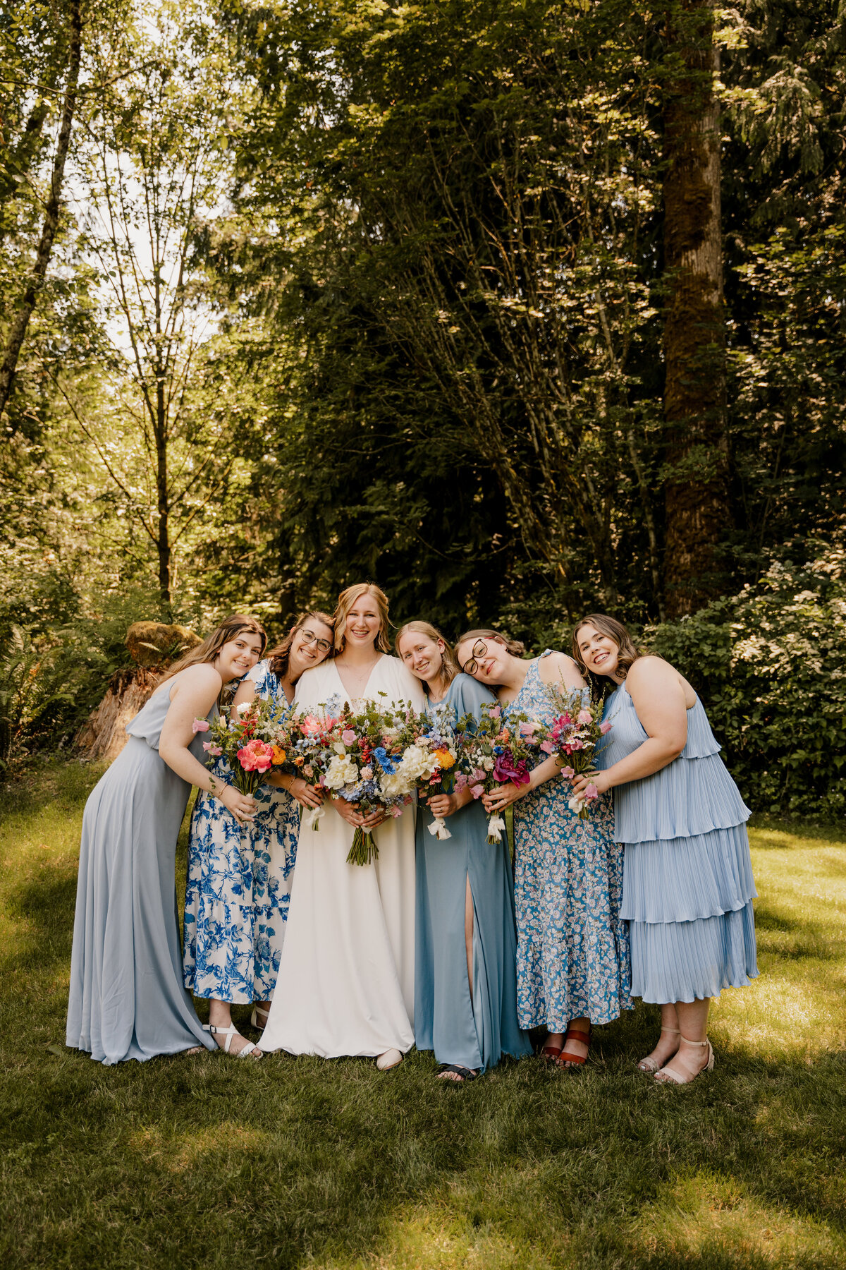 The bridesmaids lean in close to the bride in their floral blue dresses.
