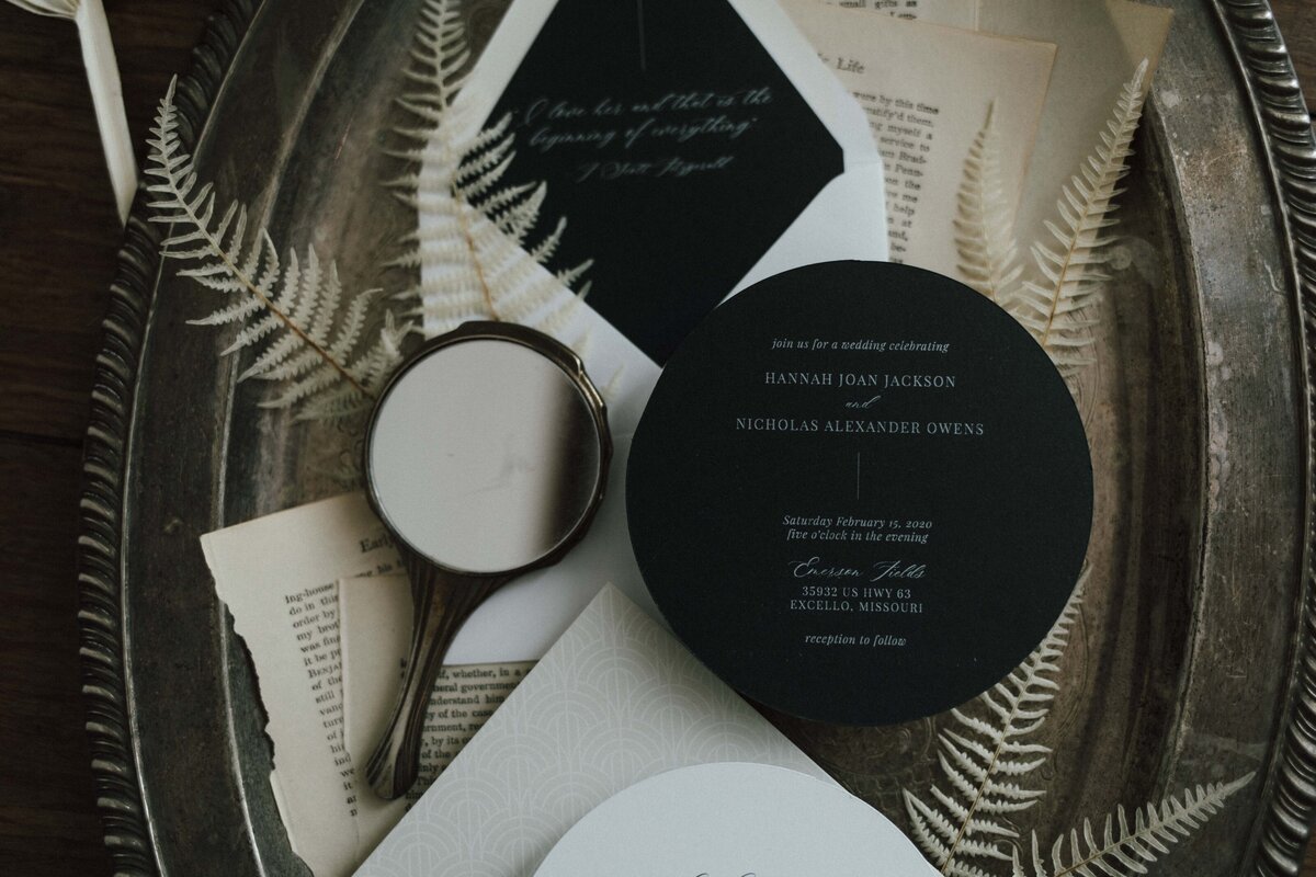 Rounded dark green wedding invitation with white cursive font paired with a white envelope on a silver tray.