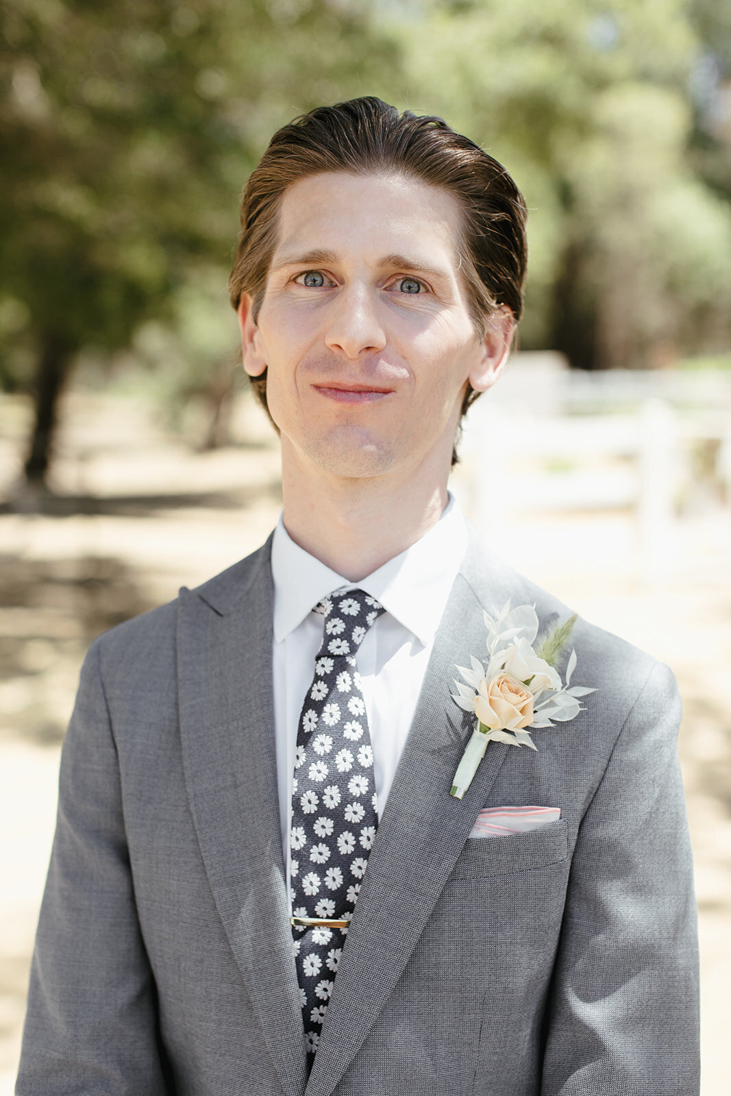 Groom poses for portrait in a grey suit, floral tie, and dried boutonniere.