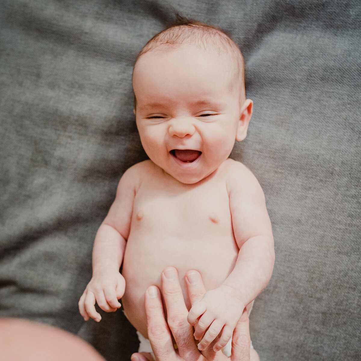 An overhead photo of the happiest baby boy! Dad is playing with his naked tummy and he is smiling and laughing.
