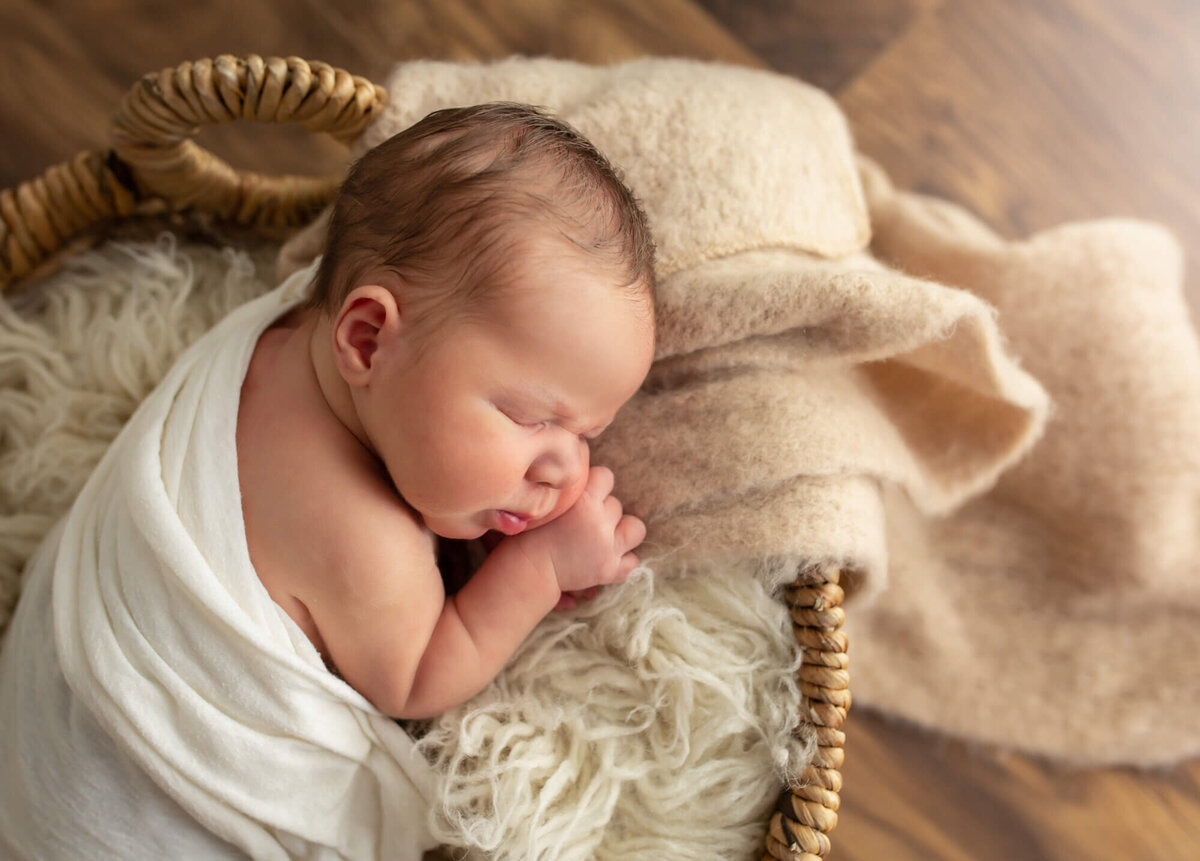 a newborn baby boy with big cheeks sleeps in a basket
