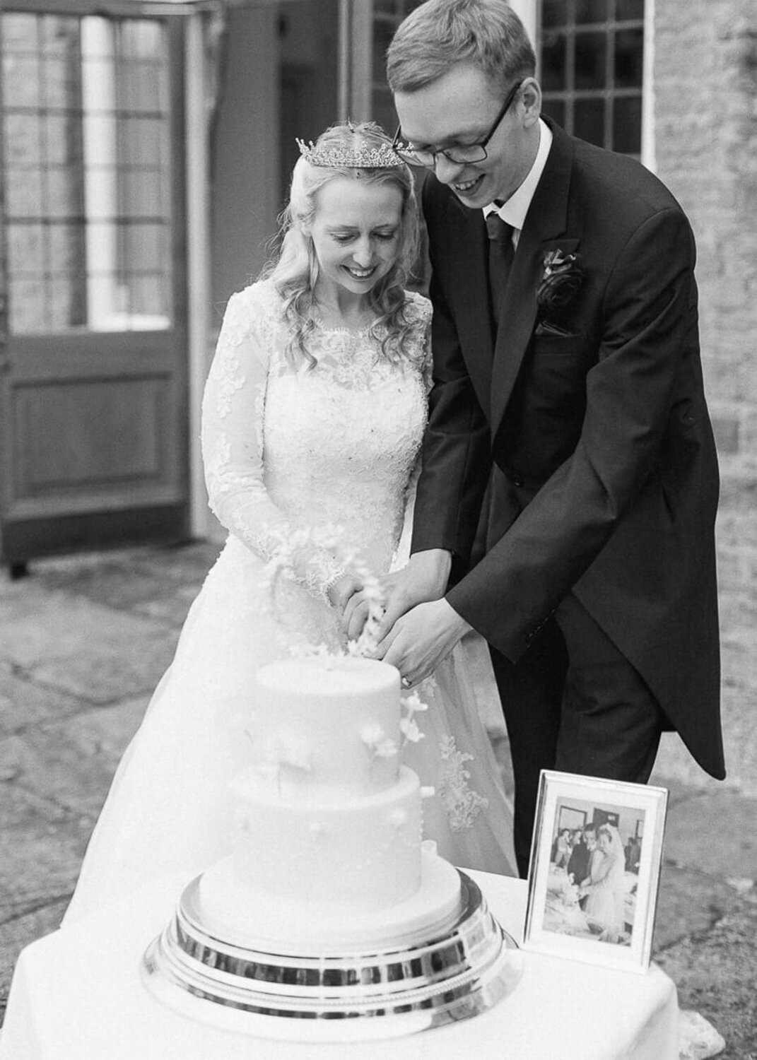 bride and groom cutting two tier wedding cake while black and white grandparents photograph has displayed on the cake table