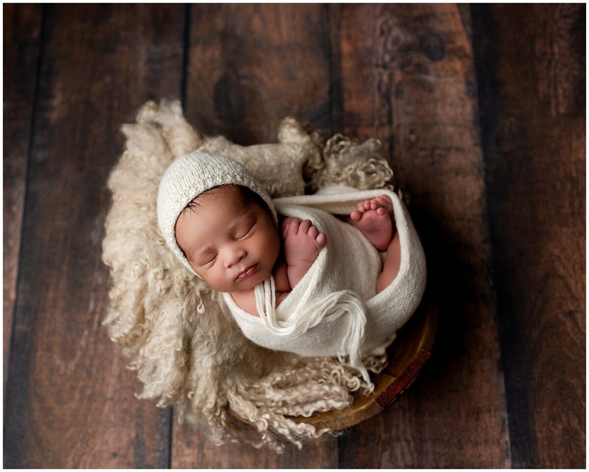 A newborn baby boy nestled in a soft, felted fabric, showcasing their tiny size and the coziness of the setting.