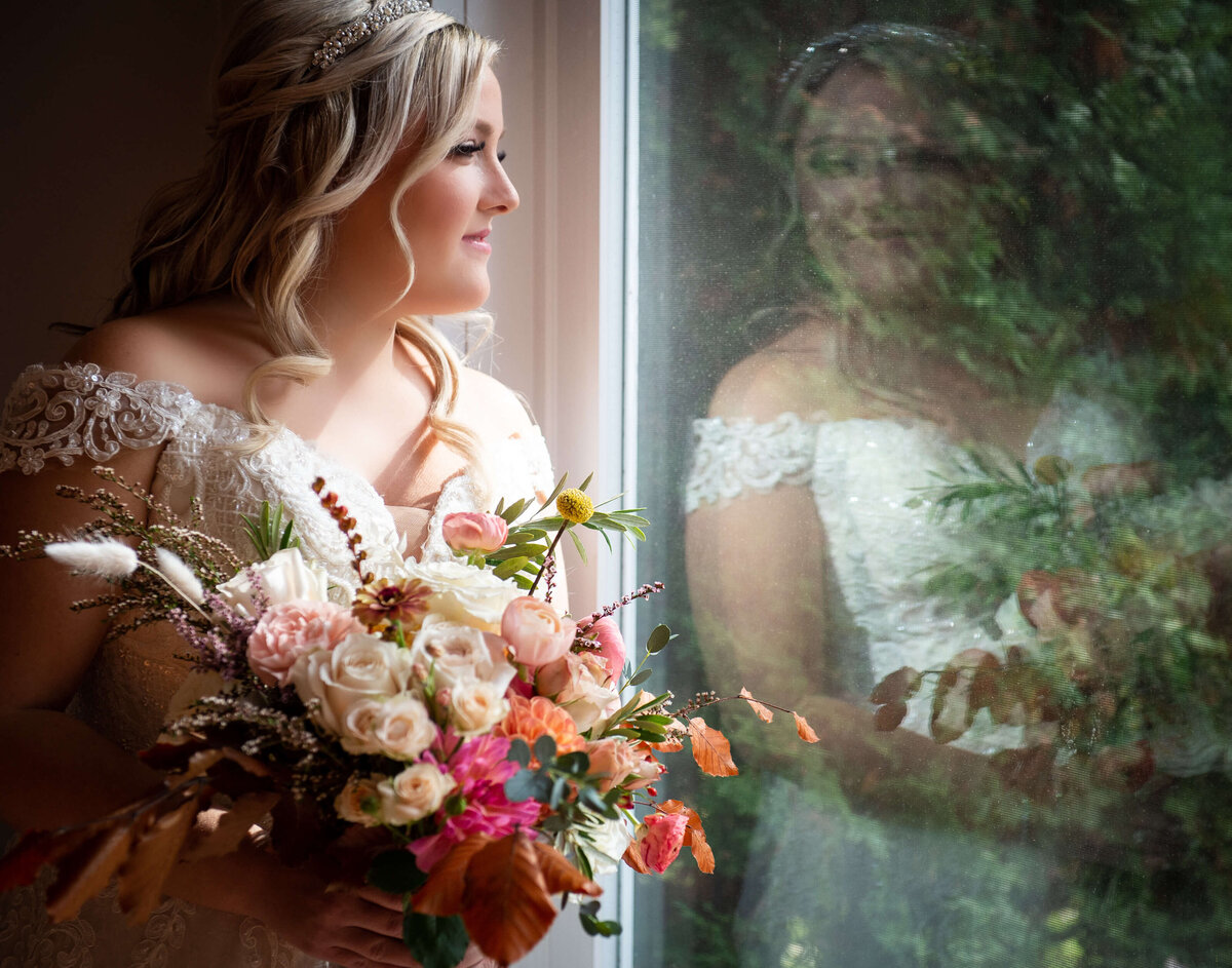 Ottawa wedding photography showing a bride looking out the window holding her fall coloured bouquet as she gets ready for her wedding at Strathmere venue