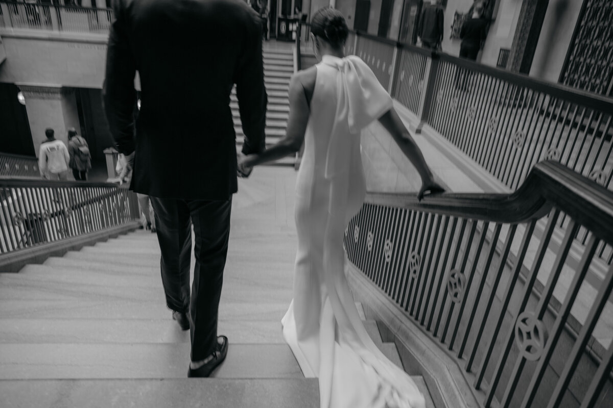 Black and white image of groom holding bride's hand as they walk down steps