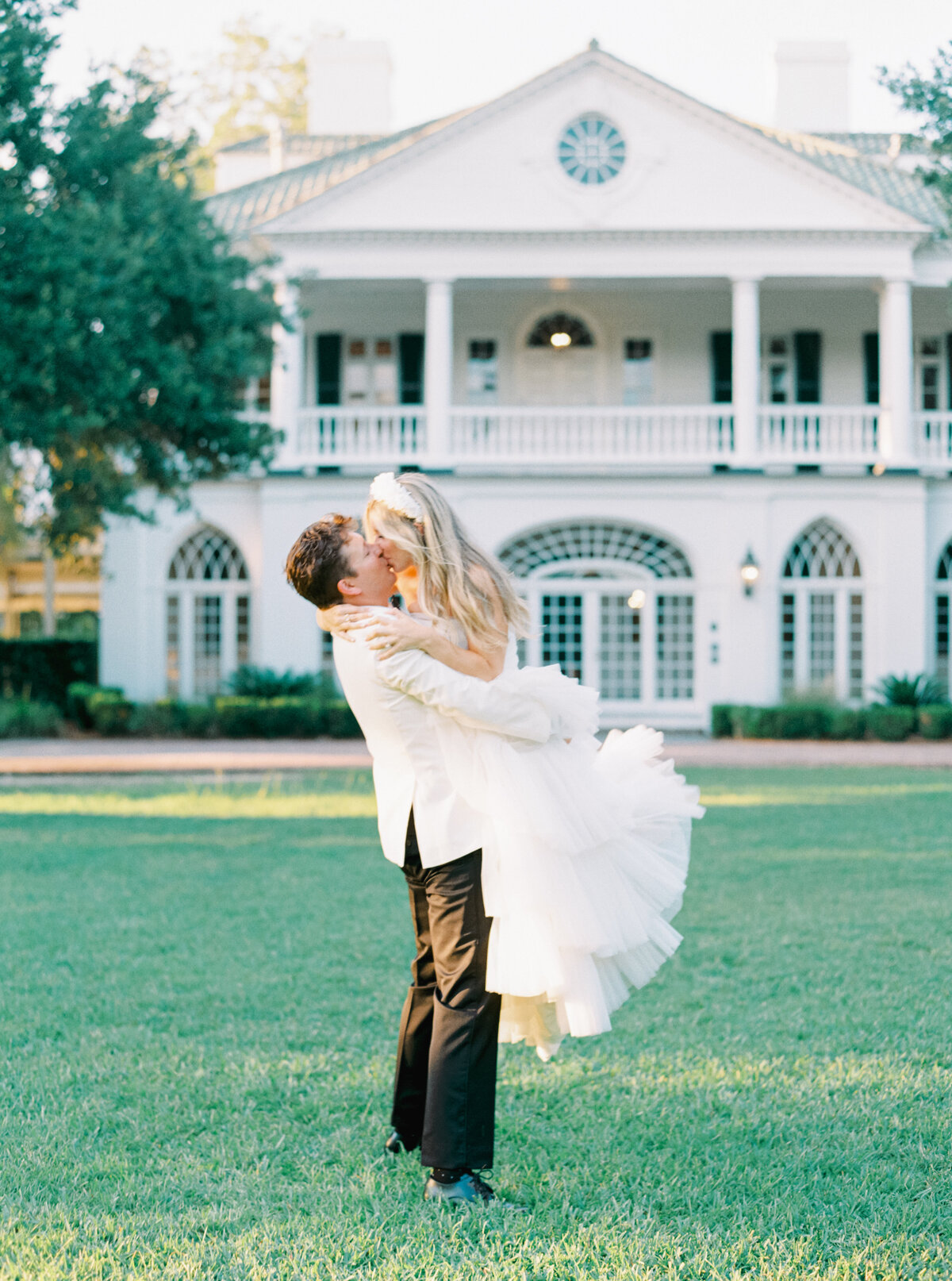 This interior designers wedding at Lowndes Grove is a must-see! Golden sunset light with groom picking up bride for a kiss. Charleston destination wedding photographer.
