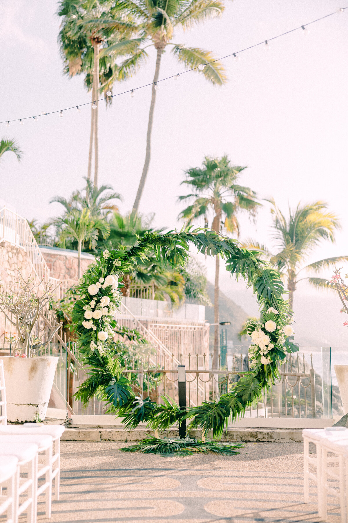 Destination Wedding Photographer captures a floral archway at an outdoor wedding venue with palm trees and string lights in the background.