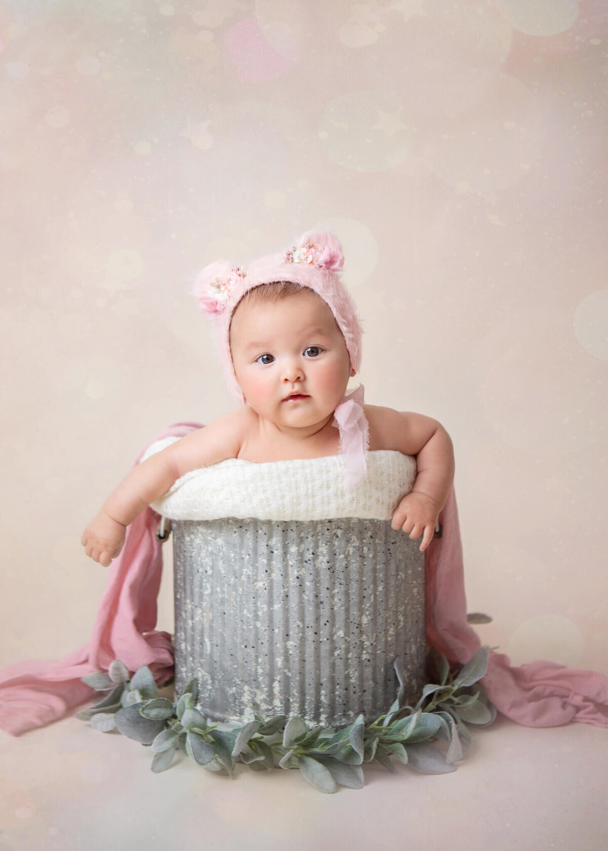 6 month old baby sitting in a bucket with a pink teddy bear hat on - - By Los Angeles Newborn Photographer
