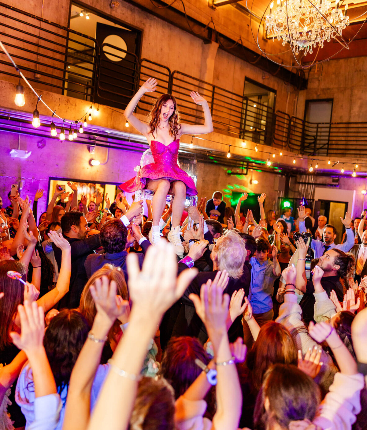 Bellevue Bar and Bat Mitzvah Photography of a teen girl in a pink dress sitting in a chair being lifted above a crowded dance floor