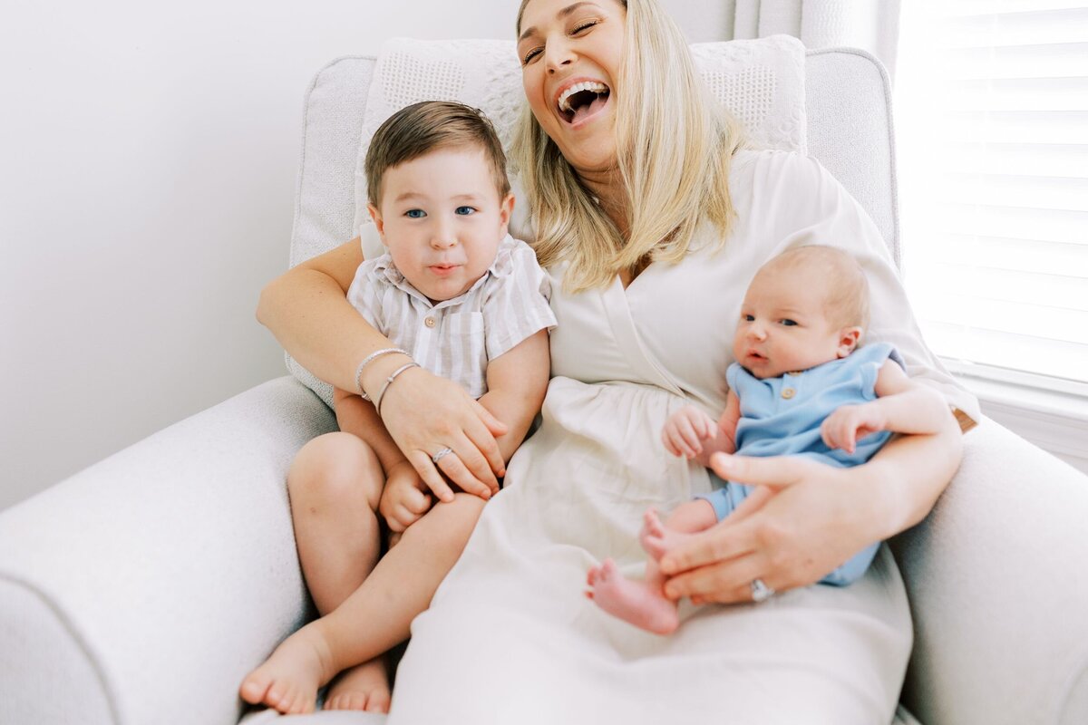 Mom laughing in rocker with toddler and new baby