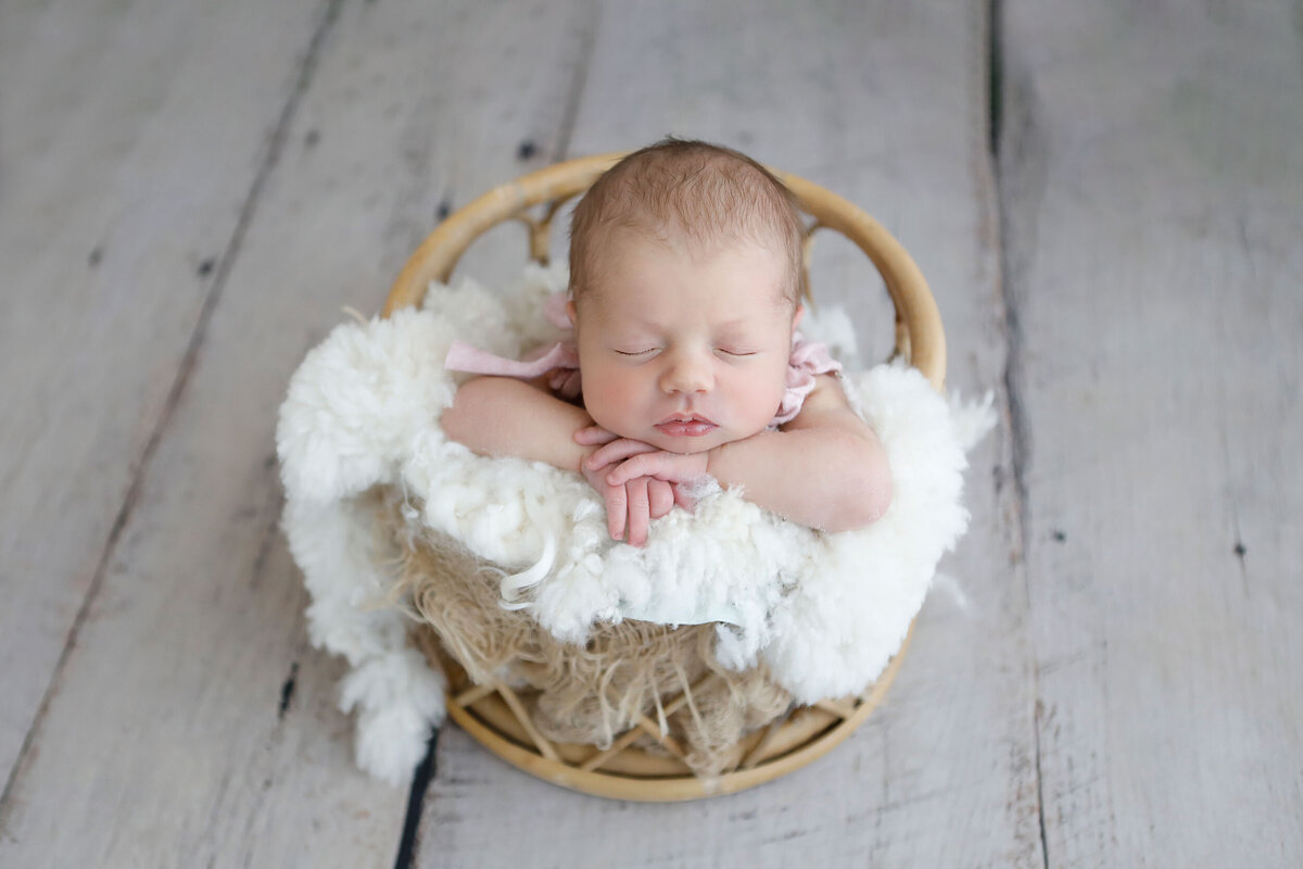 lovely-little-girl-sleeping-in-a-bamboo-basket-for-her-newborn-shoot