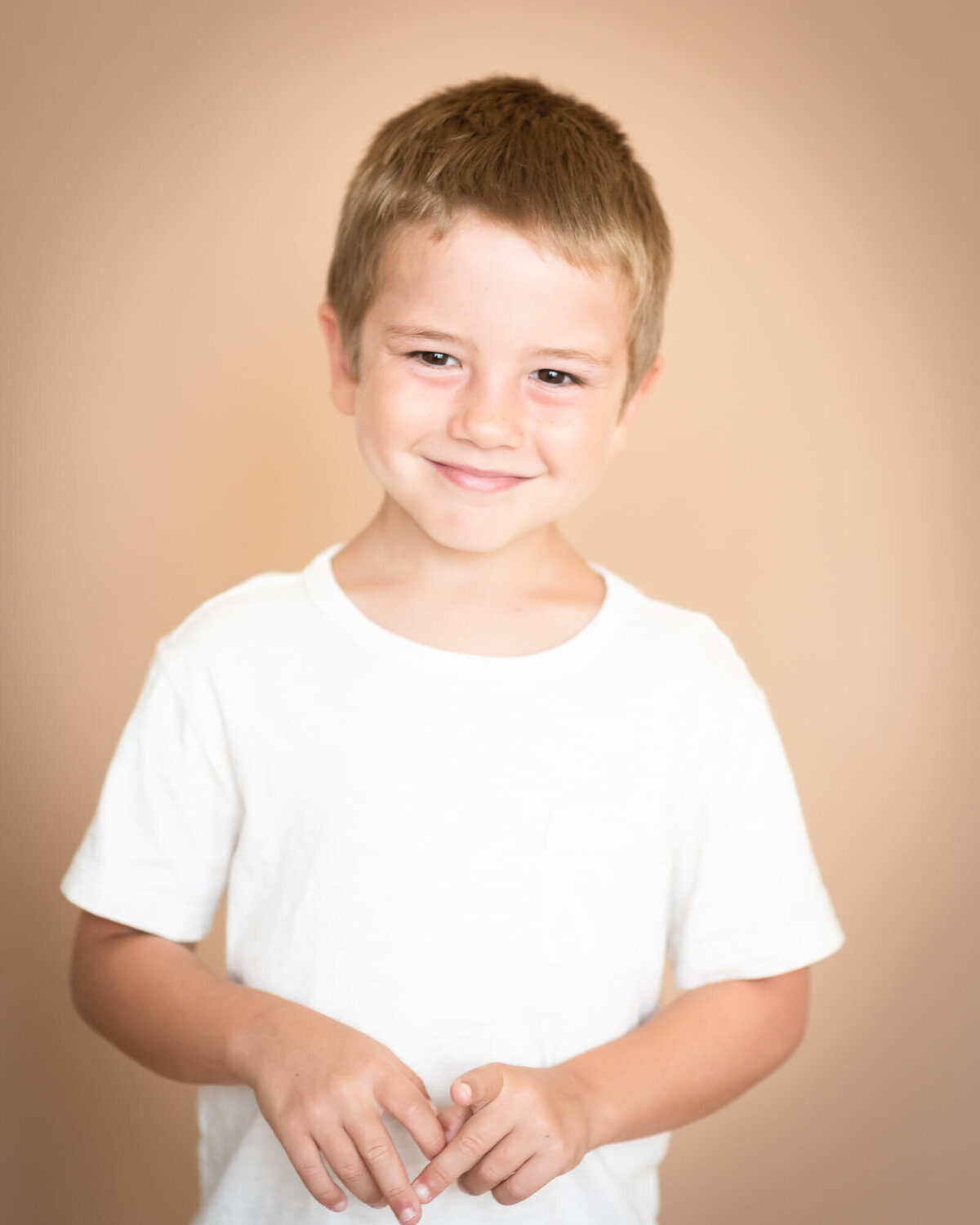 adorable young boy smiling wearing white tee shirt with a tan background