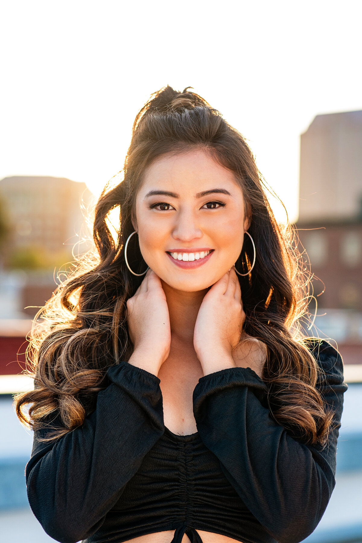 Close up portrait of senior girl smiling on rooftop at sunset.