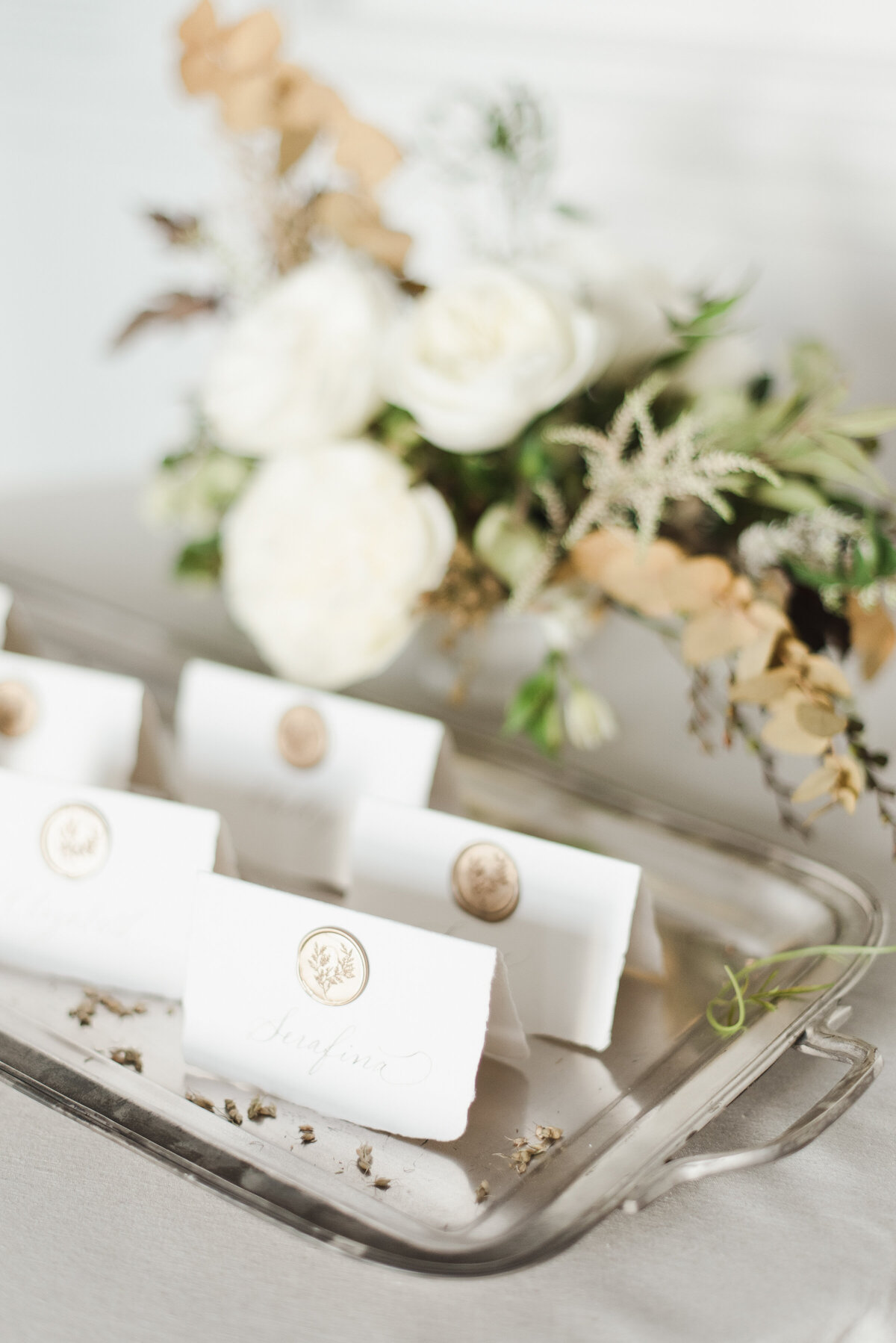 A close-up of a tray displaying tented white place cards made from handmade paper. Each card features delicately hand-calligraphed names and is sealed with a gold wax seal.