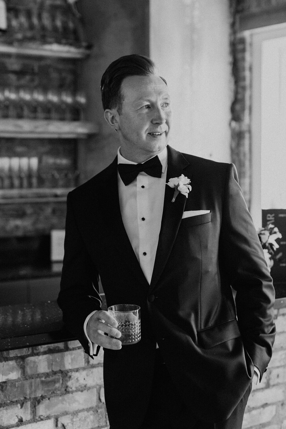 Black and white photo of groom with a cocktail in his tuxedo.