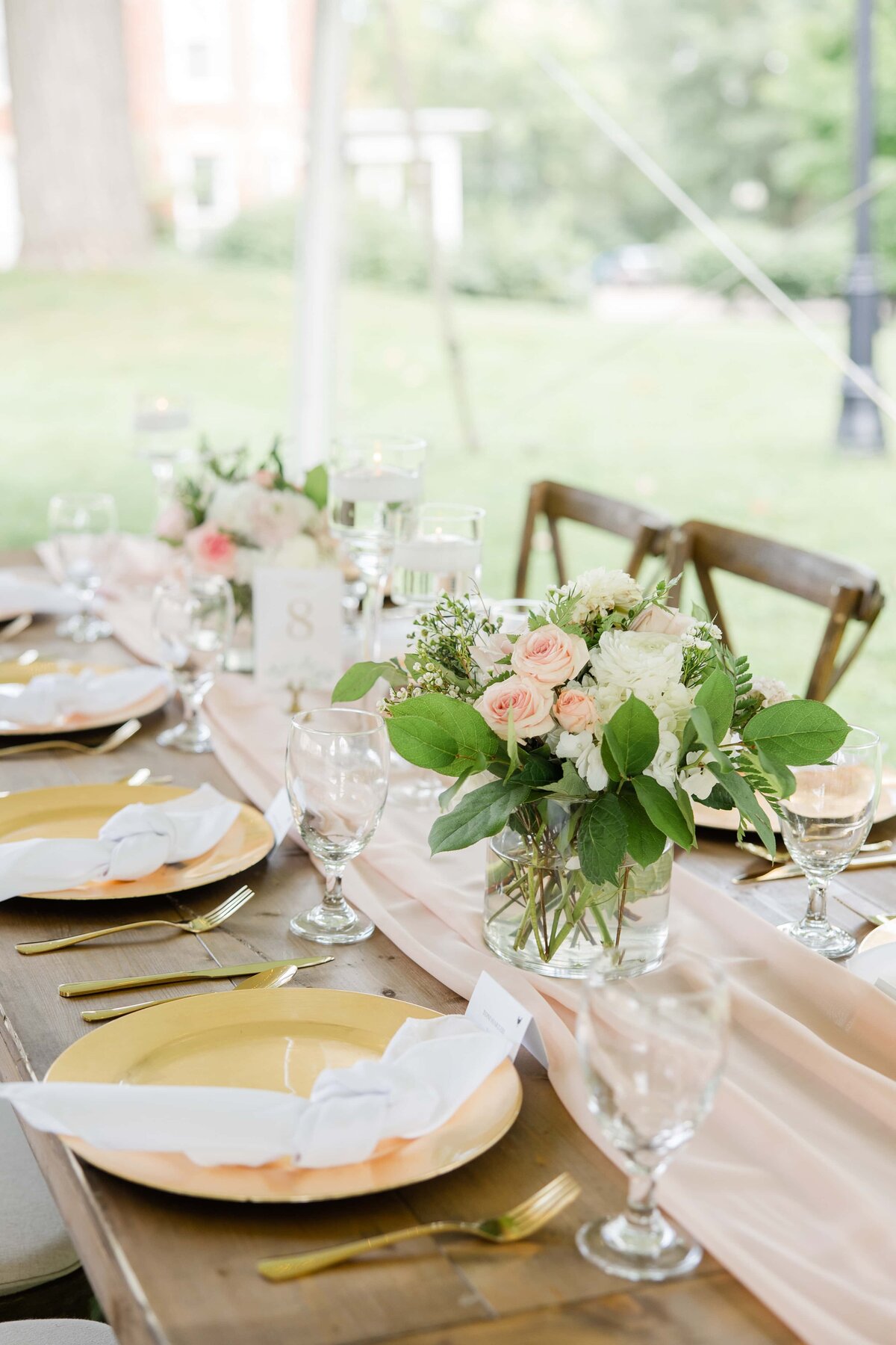 Elegant outdoor wedding table setting with gold plates, floral centerpieces, and crystal glassware arranged on a wooden table at an Iowa winery.