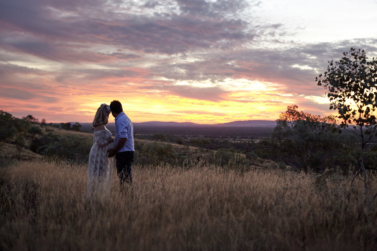 Pregnant wife and husband embracing and looking at the sunset in natural bushland