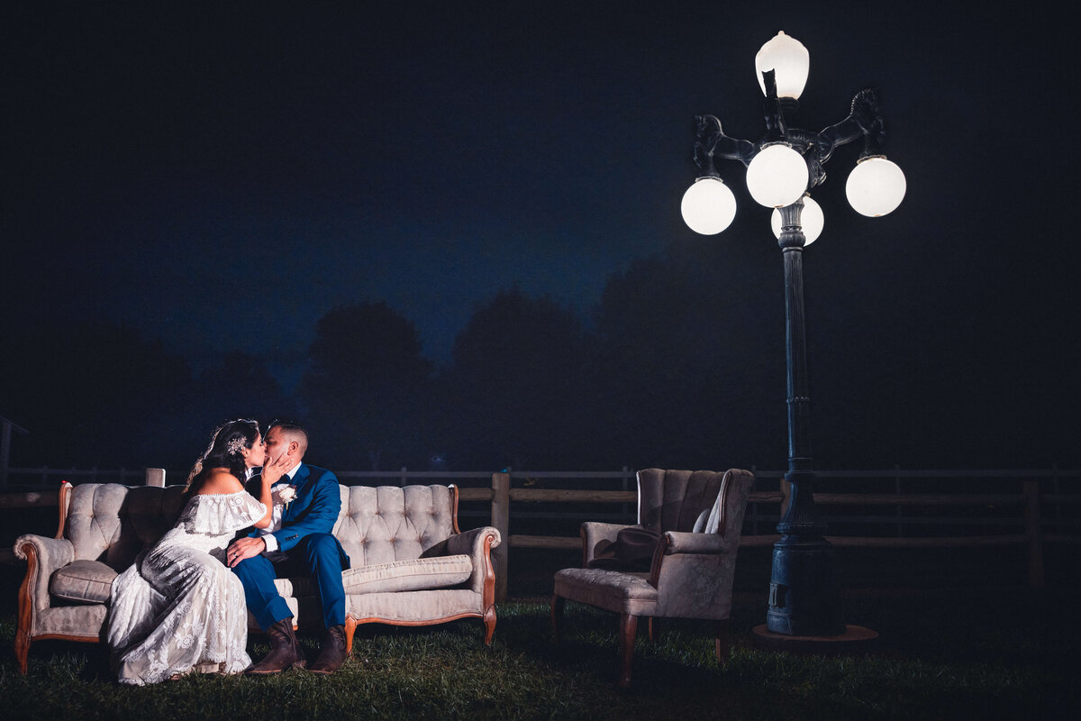 Couple sitting on couch kissing with large bulb lamp nearby