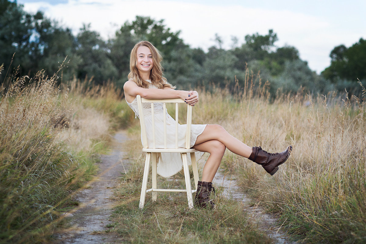 Girl kicks up her cowboy boots sitting in a vintage chair in a field