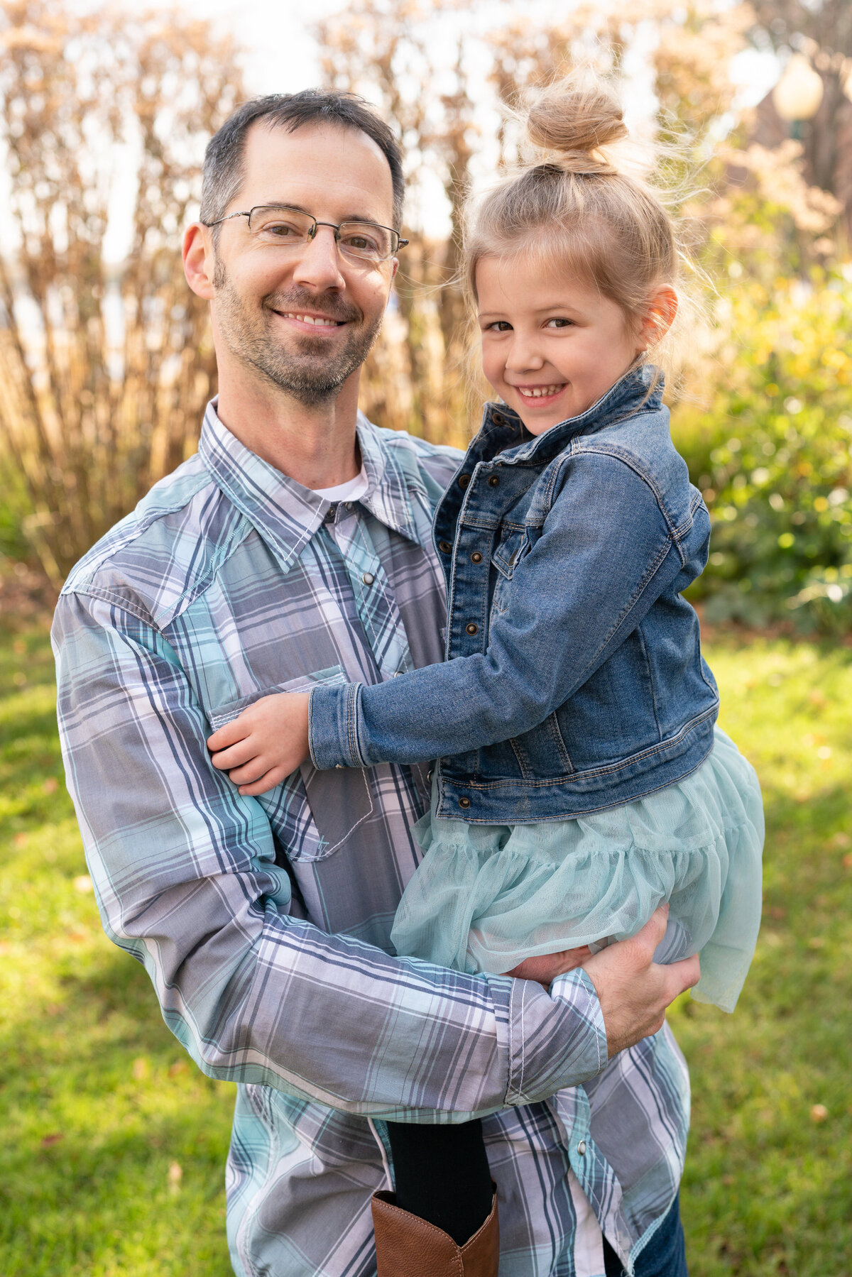Dad holds daughter dressed in denim jacket and cowboy.