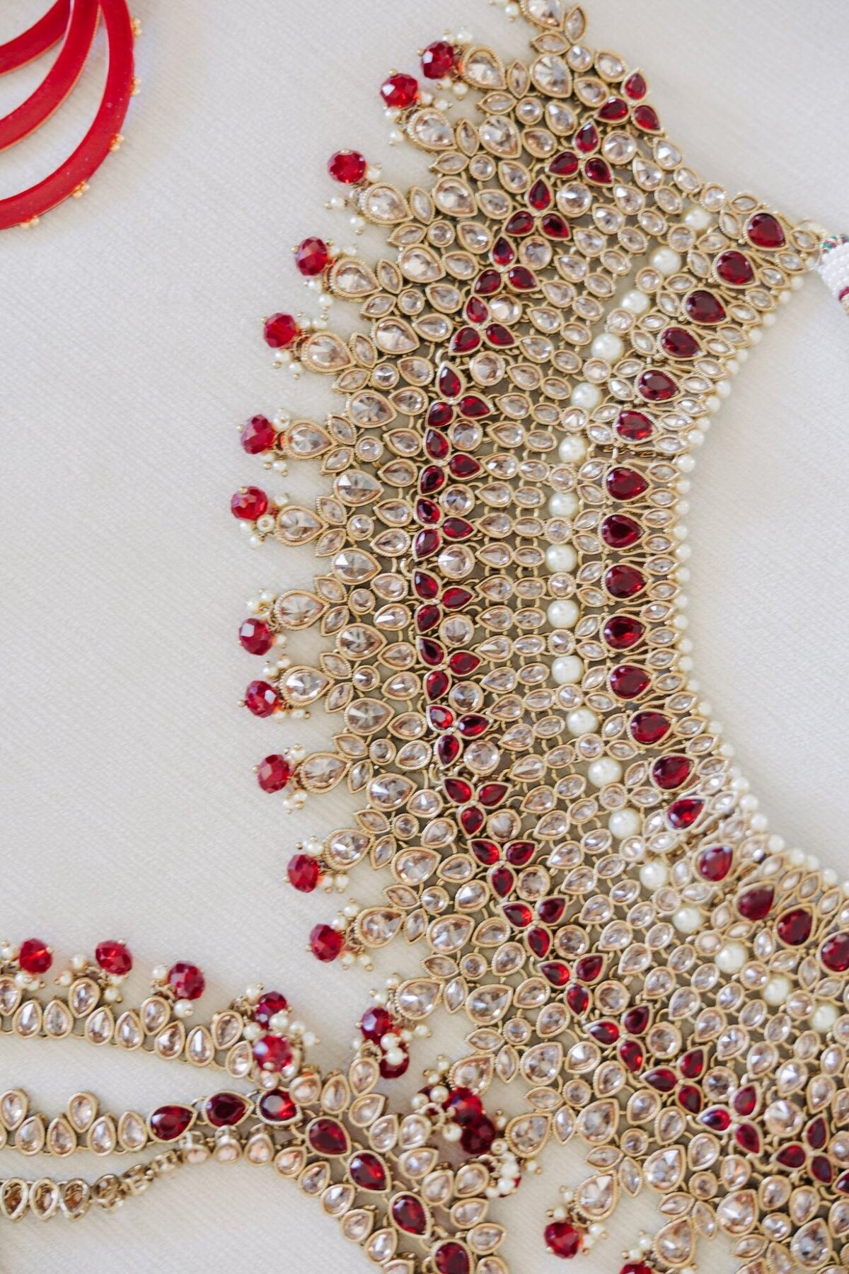 Detailed close-up of an intricate beaded and jeweled embroidery on fabric, featuring gold beads and red gemstones.