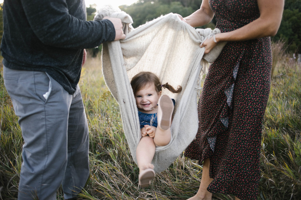Mom and dad carrying little girl in a blanket during sunset session with Elle Baker Photography