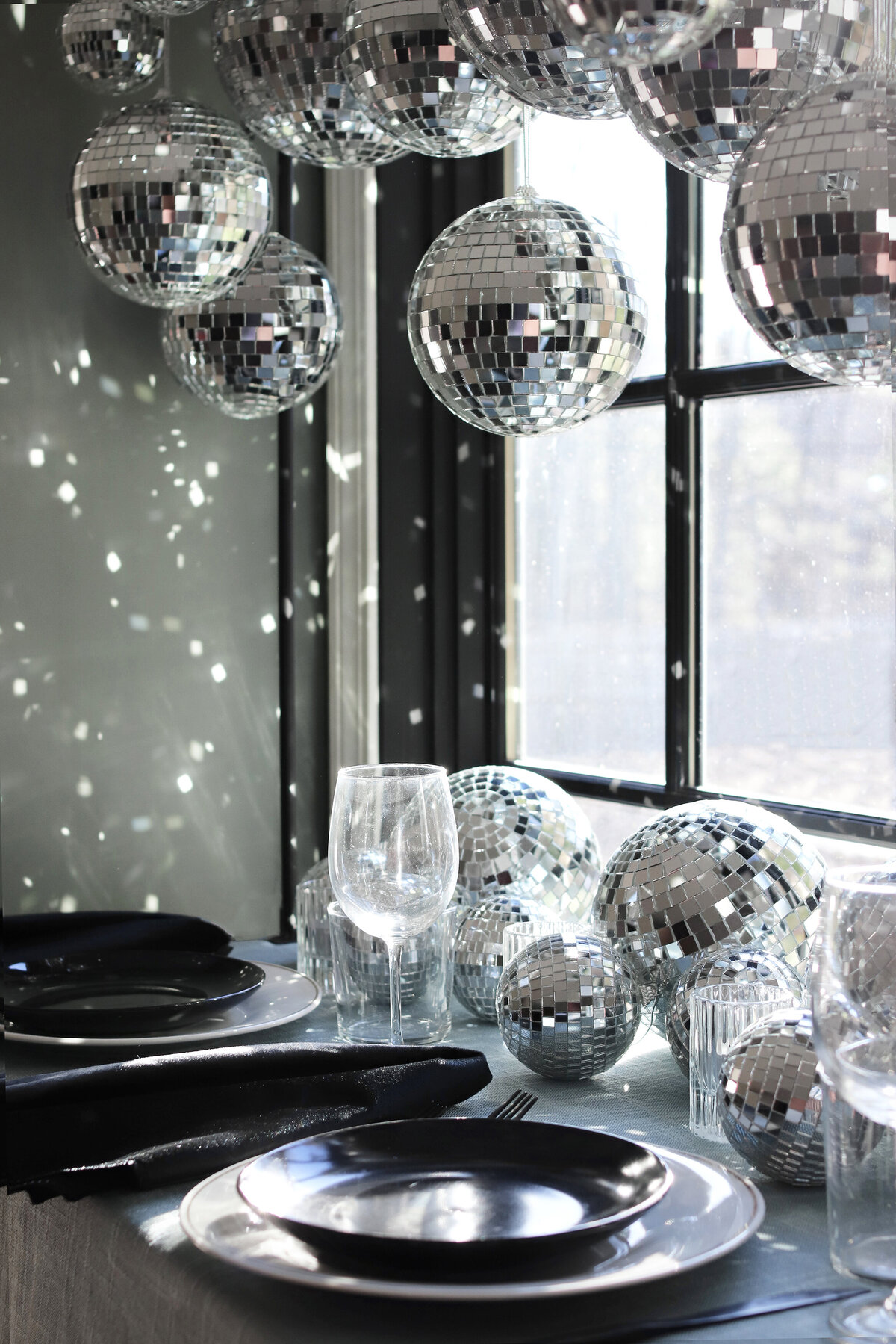 Different sized disco balls hanging near a window above a table set with black china