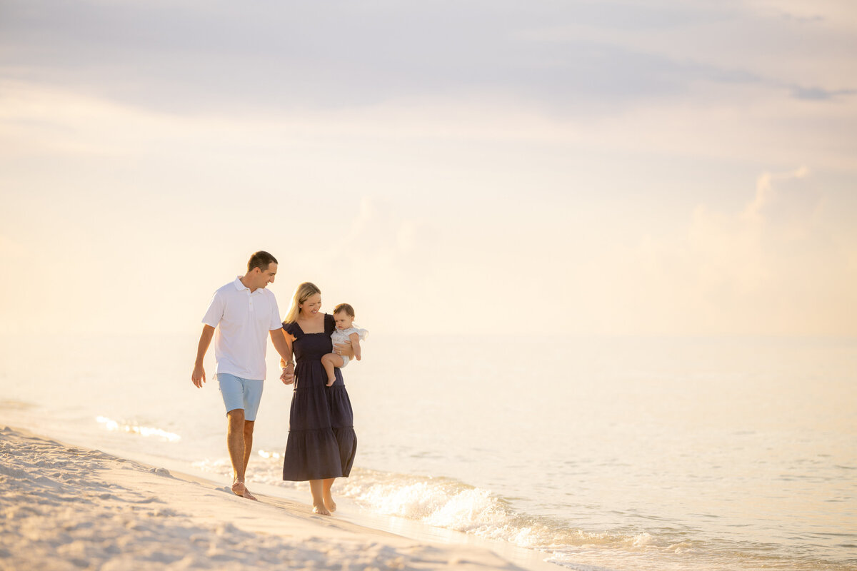 Near Watercolor Inn,  a family of three walking along the water's edge at sunset