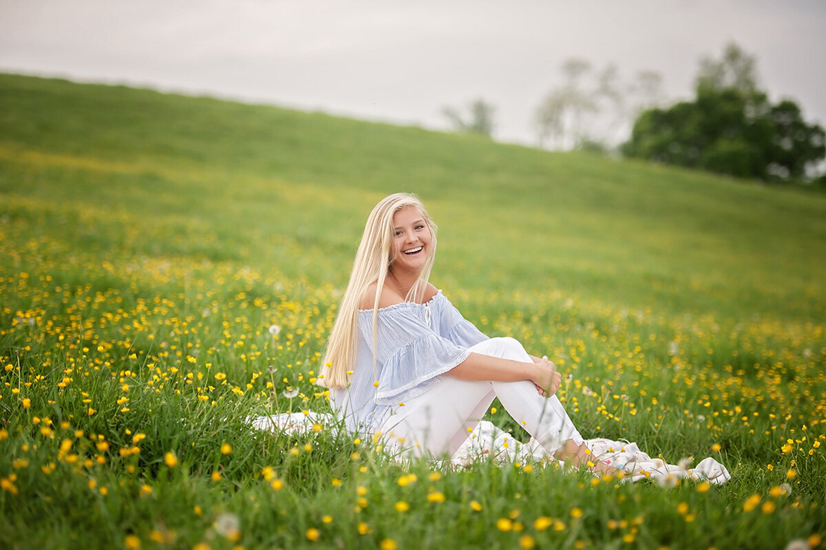 Senior session of young woman sitting in a field of flowers