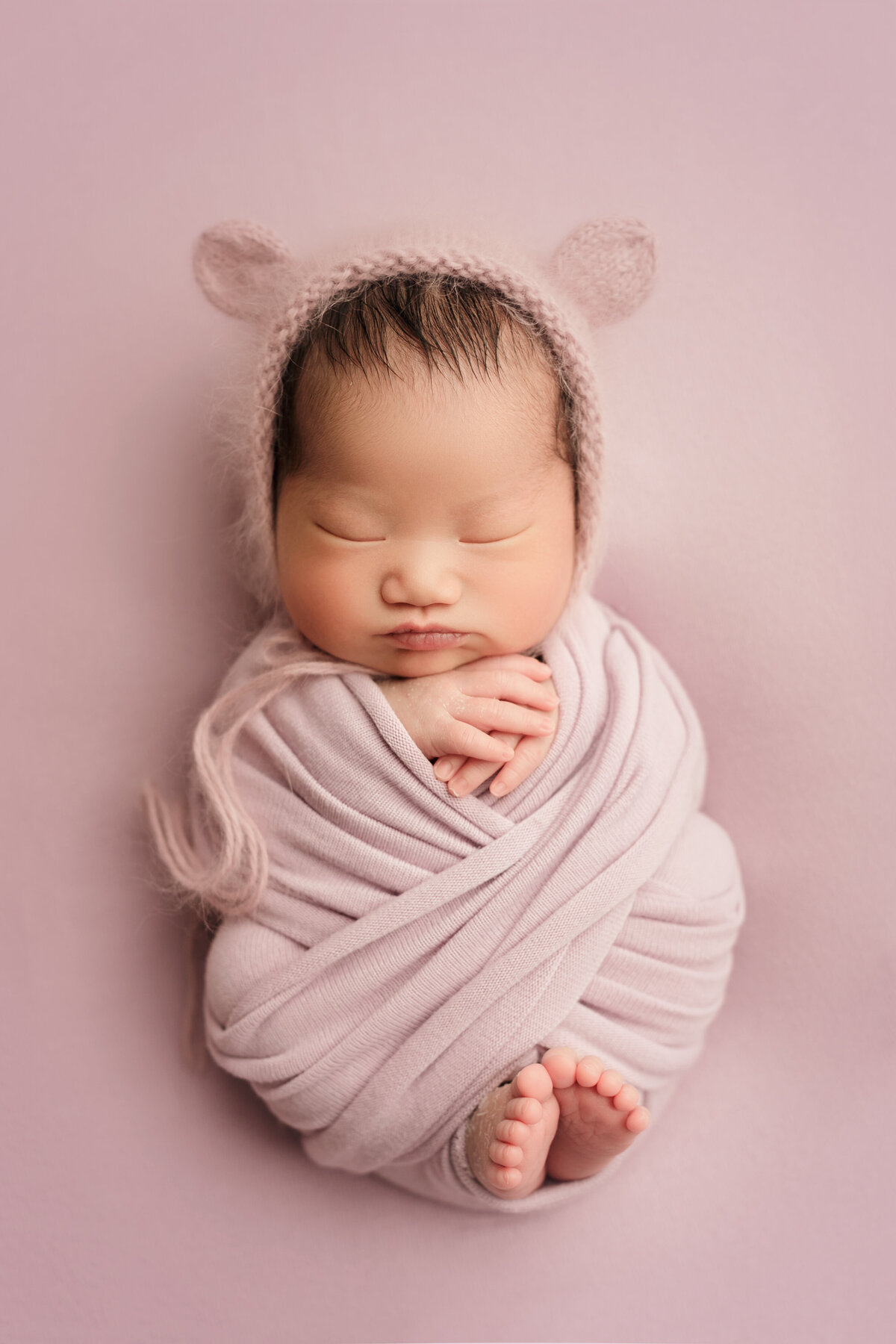newborn baby girl on lavendar blanket with a  bear hat on