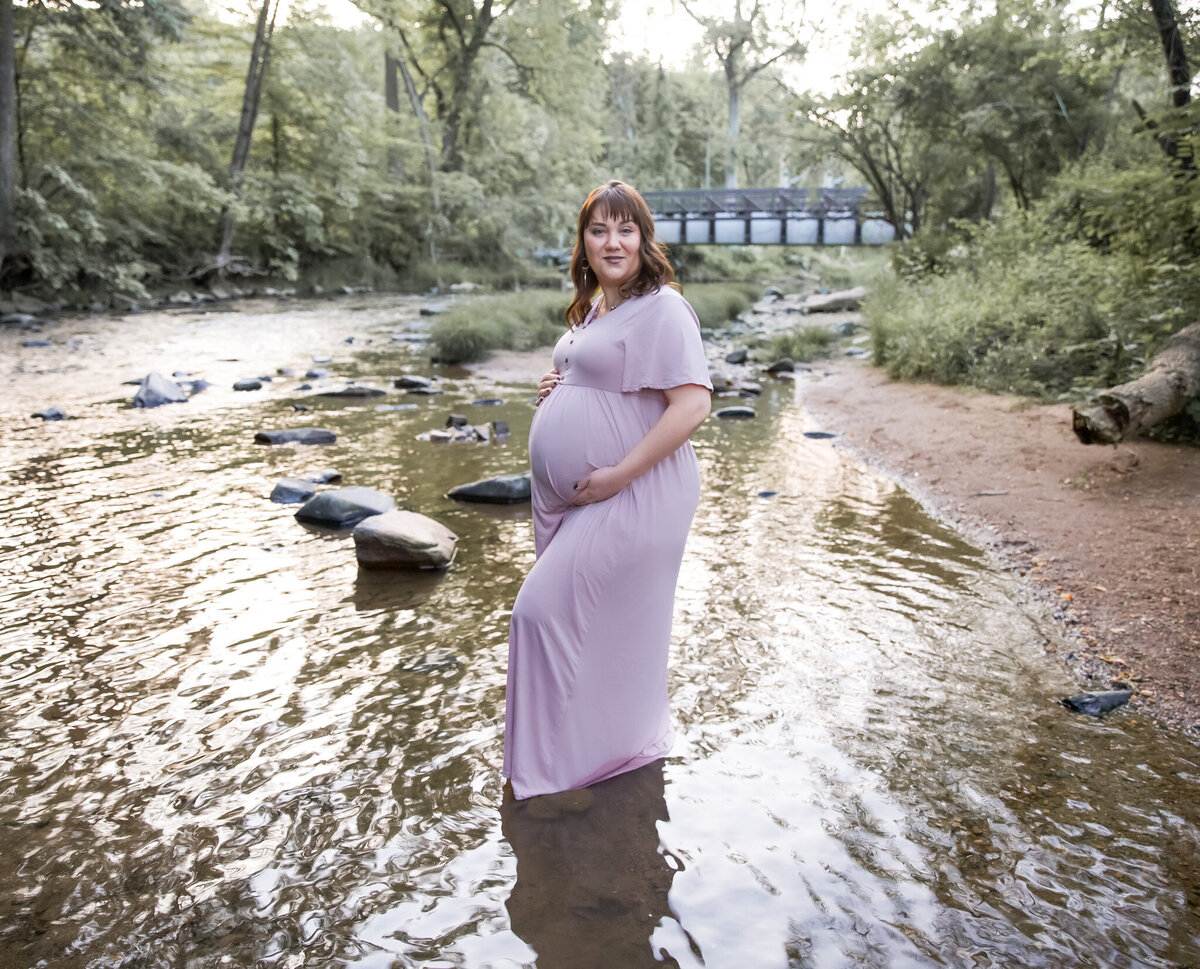 A Baltimore County Mom holds her baby bump during her pregnancy photos in a stream.