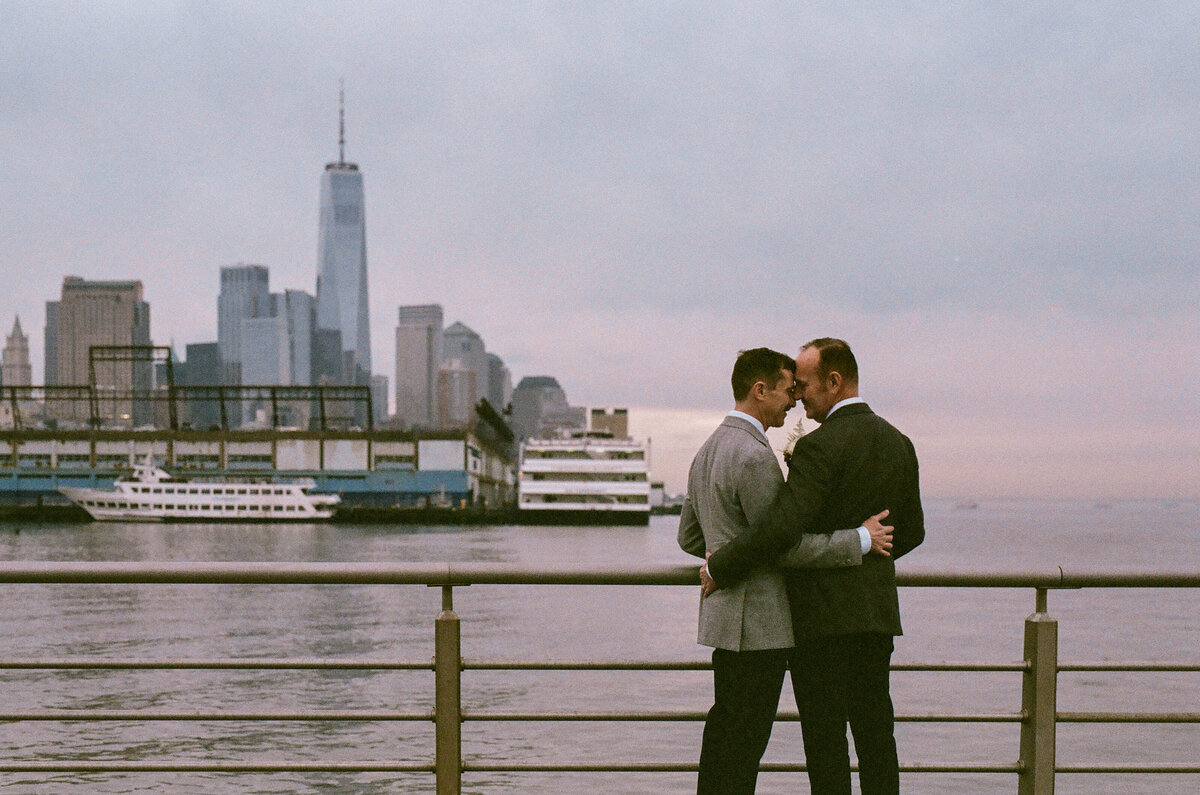 A couple leaning their foreheads against each other overlooking the water.